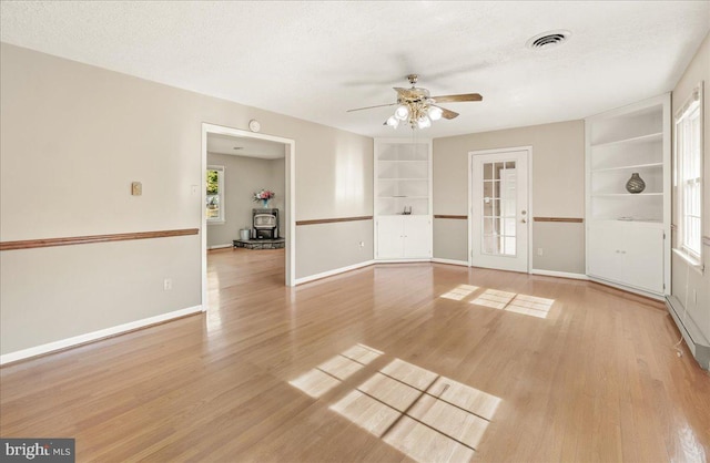 unfurnished living room featuring ceiling fan, a textured ceiling, light hardwood / wood-style flooring, and built in shelves