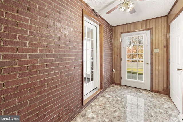 doorway featuring ceiling fan, brick wall, a textured ceiling, and plenty of natural light