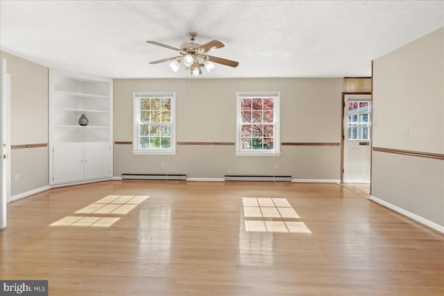 empty room featuring light hardwood / wood-style floors, a textured ceiling, baseboard heating, and built in shelves