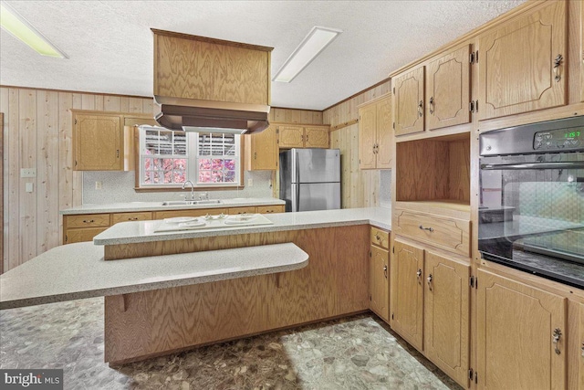 kitchen featuring oven, sink, a textured ceiling, wooden walls, and stainless steel refrigerator