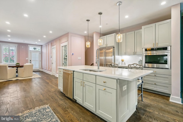 kitchen with dark wood-type flooring, appliances with stainless steel finishes, sink, and a kitchen island with sink