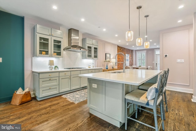 kitchen featuring dark wood-type flooring, wall chimney exhaust hood, sink, and a center island with sink