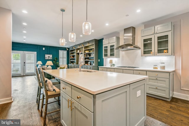 kitchen featuring sink, a kitchen island with sink, wall chimney range hood, and dark hardwood / wood-style floors