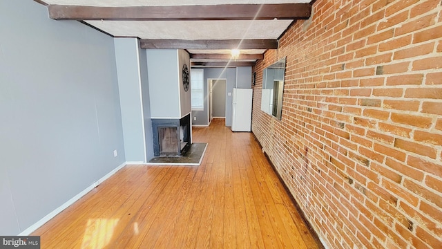 hall featuring light wood-type flooring, brick wall, and beam ceiling