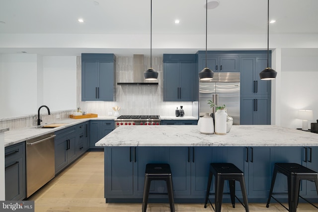 kitchen with stainless steel appliances, a kitchen bar, pendant lighting, and wall chimney exhaust hood