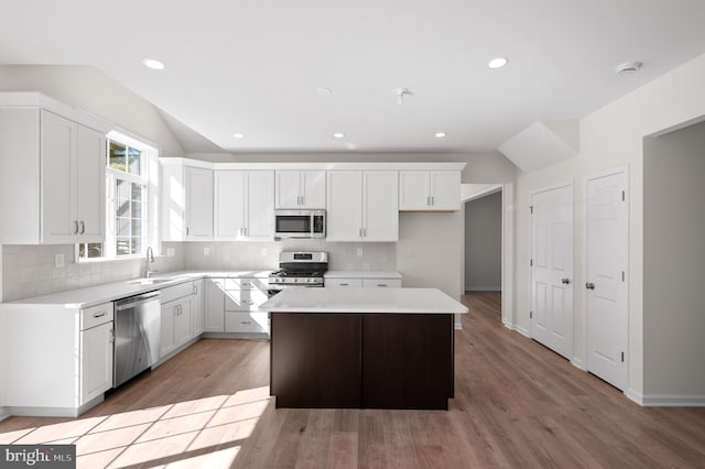 kitchen with appliances with stainless steel finishes, white cabinets, hardwood / wood-style flooring, and a kitchen island