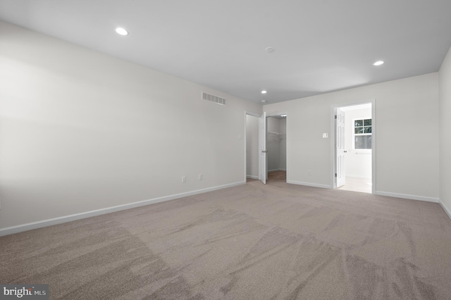 unfurnished bedroom with a walk in closet, a closet, and light colored carpet