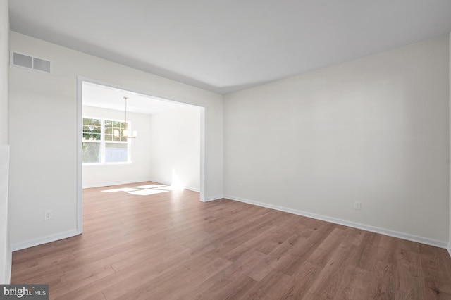 unfurnished room featuring an inviting chandelier and light hardwood / wood-style flooring