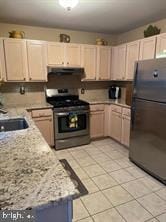 kitchen with light stone countertops, light brown cabinetry, stainless steel range, and black refrigerator