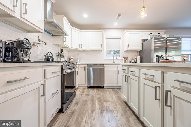 kitchen with wall chimney exhaust hood, appliances with stainless steel finishes, a sink, and white cabinetry