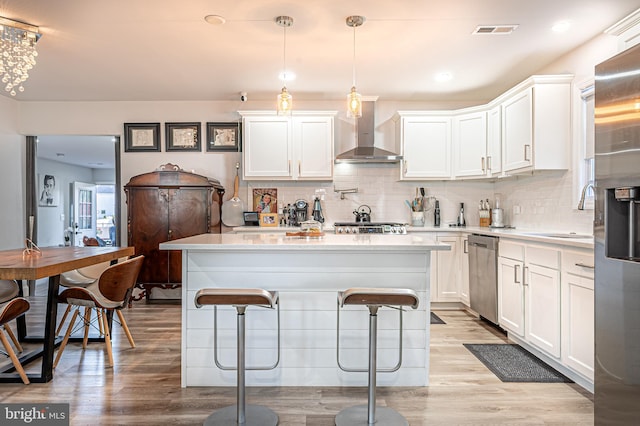 kitchen with white cabinetry, light hardwood / wood-style flooring, wall chimney exhaust hood, and appliances with stainless steel finishes