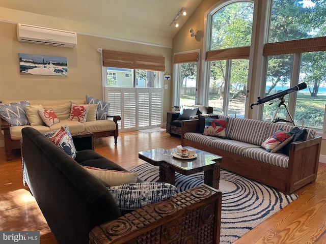 living room with a wall unit AC, track lighting, light wood-type flooring, and high vaulted ceiling