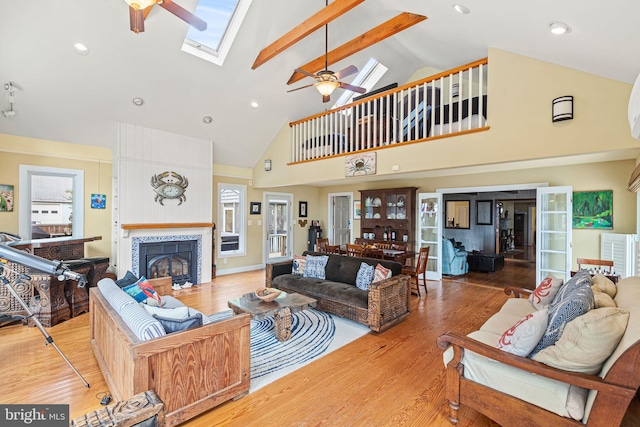 living room featuring high vaulted ceiling, light hardwood / wood-style flooring, ceiling fan, and a skylight