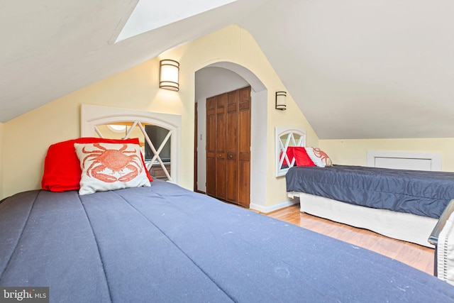 bedroom featuring vaulted ceiling with skylight, wood-type flooring, and a closet