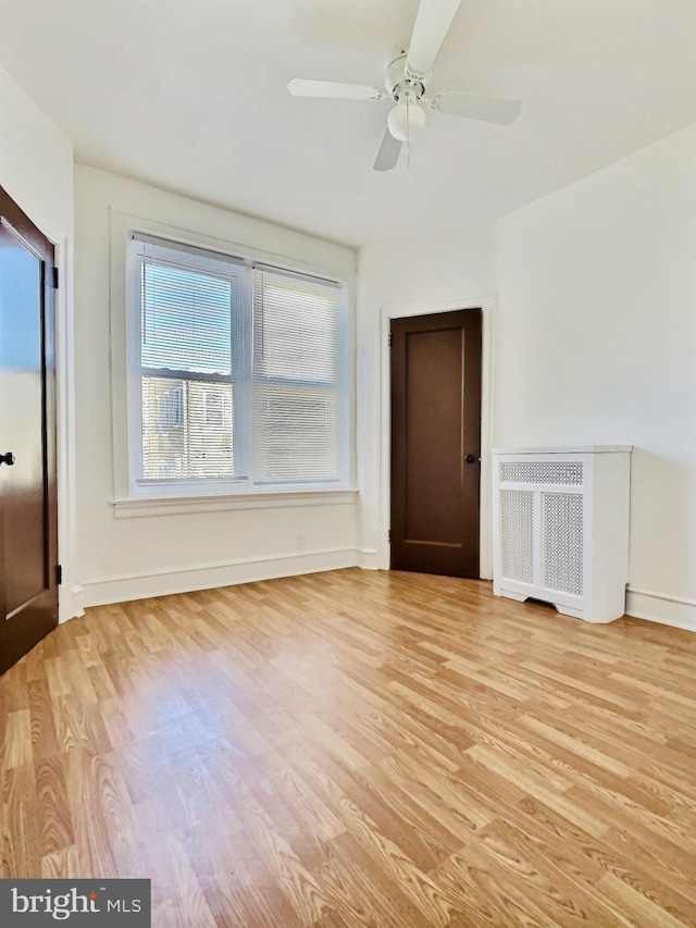 unfurnished room with radiator, light hardwood / wood-style floors, and ceiling fan