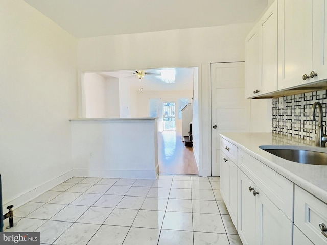 kitchen featuring backsplash, sink, light tile patterned floors, white cabinetry, and ceiling fan