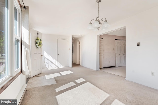 unfurnished room featuring an inviting chandelier, a baseboard heating unit, and light colored carpet