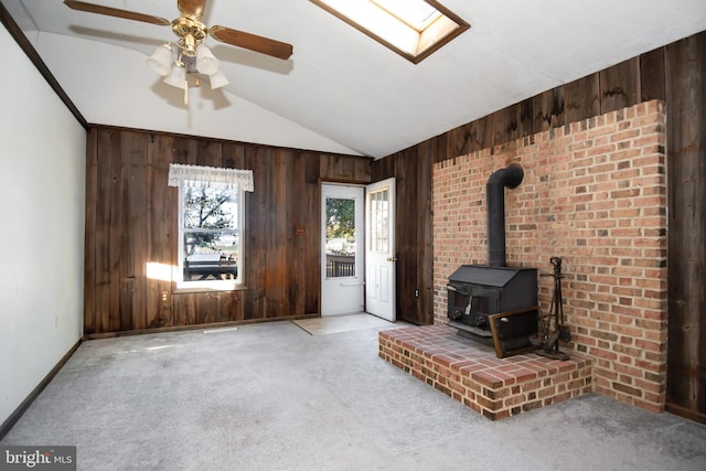 unfurnished living room featuring vaulted ceiling with skylight, a wood stove, wood walls, and light colored carpet