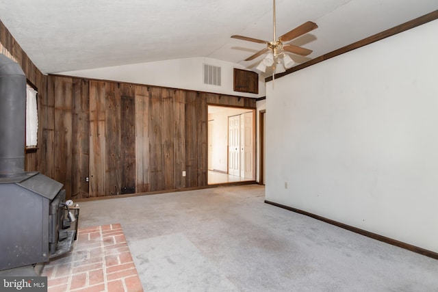 unfurnished living room featuring lofted ceiling, wooden walls, a wood stove, and ceiling fan