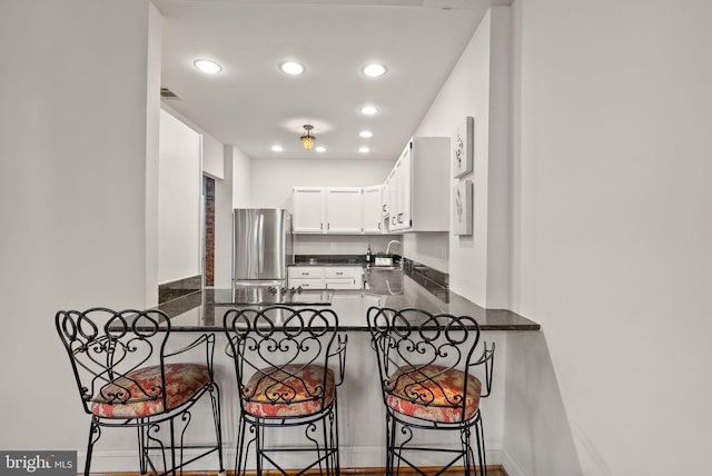 kitchen with kitchen peninsula, sink, stainless steel fridge, a breakfast bar, and white cabinets