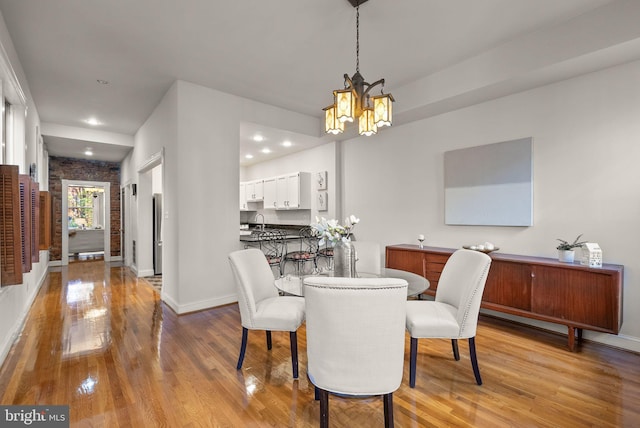 dining room featuring light hardwood / wood-style floors, an inviting chandelier, sink, and brick wall