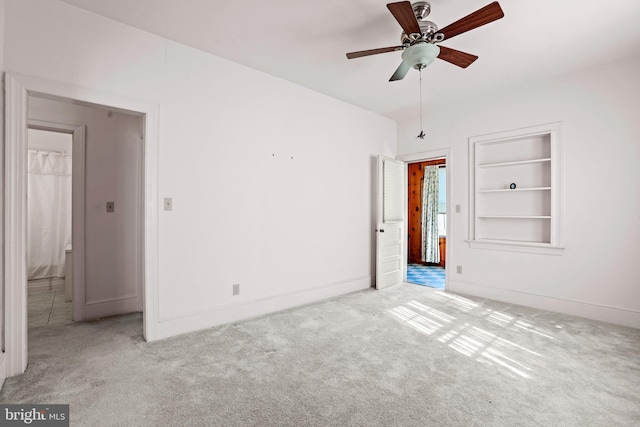 empty room with light carpet, built in shelves, and ceiling fan