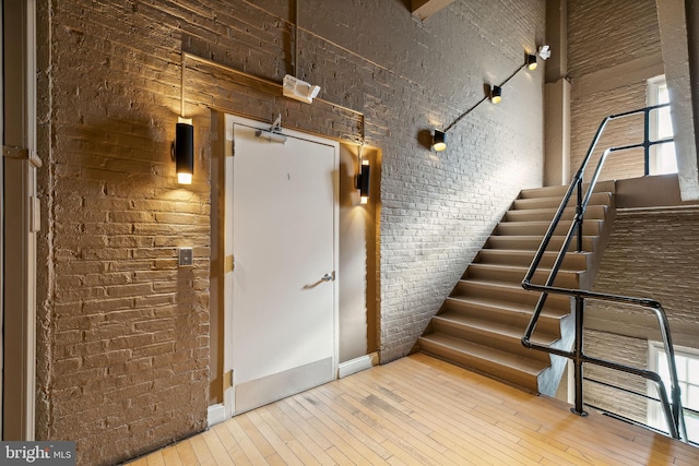 staircase featuring hardwood / wood-style floors, brick wall, and a high ceiling