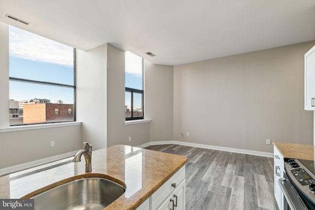 kitchen featuring stainless steel electric range, white cabinets, sink, light stone countertops, and light wood-type flooring