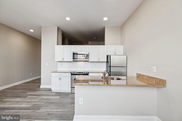 kitchen with light hardwood / wood-style floors, stainless steel appliances, kitchen peninsula, sink, and white cabinetry