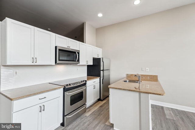 kitchen with white cabinetry, sink, appliances with stainless steel finishes, light stone countertops, and light hardwood / wood-style flooring