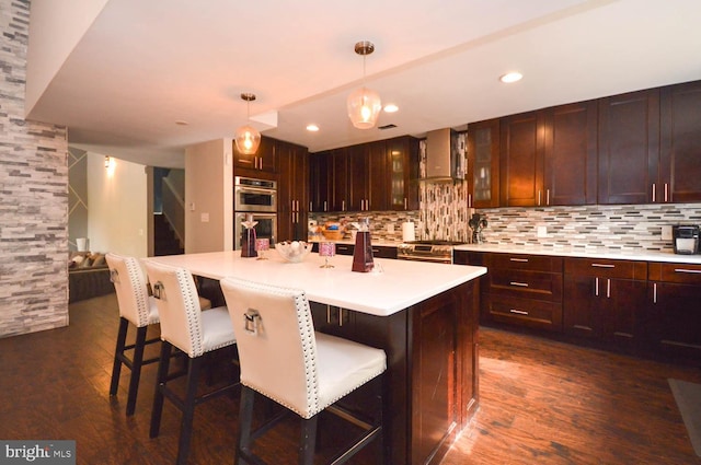 kitchen with an island with sink, appliances with stainless steel finishes, decorative light fixtures, and dark hardwood / wood-style flooring