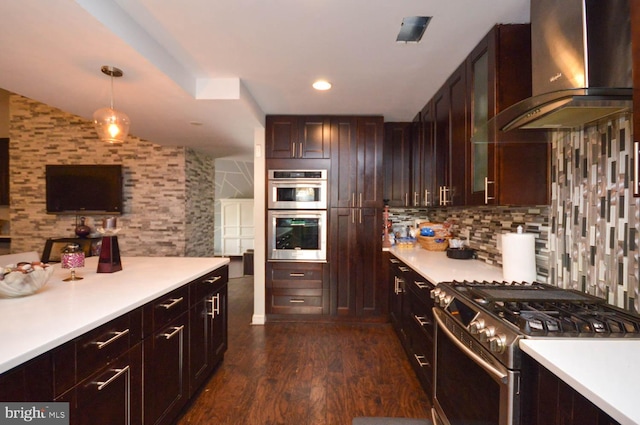 kitchen featuring tasteful backsplash, stainless steel appliances, pendant lighting, dark wood-type flooring, and wall chimney exhaust hood