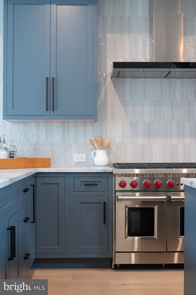 kitchen with wall chimney range hood, tasteful backsplash, light hardwood / wood-style floors, and premium stove