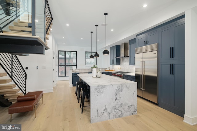 kitchen with a breakfast bar area, a kitchen island, pendant lighting, wall chimney exhaust hood, and premium appliances