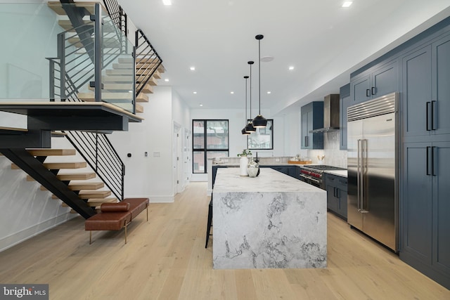 kitchen with wall chimney exhaust hood, hanging light fixtures, a center island, light wood-type flooring, and premium appliances