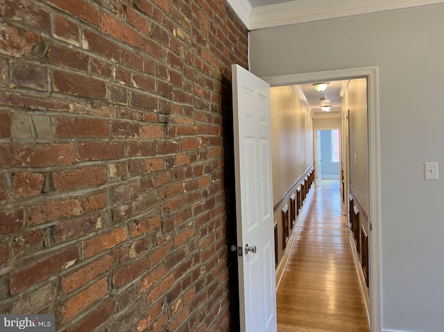 hallway featuring light hardwood / wood-style floors, brick wall, and ornamental molding