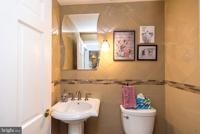 bathroom featuring toilet, tile walls, and sink