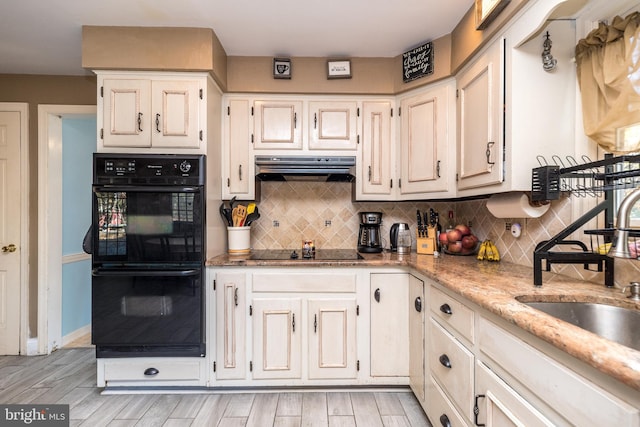 kitchen with tasteful backsplash, light stone counters, sink, black appliances, and light hardwood / wood-style flooring