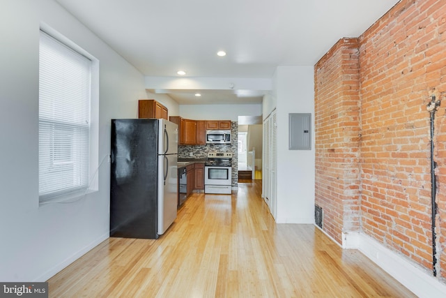 kitchen featuring brick wall, electric panel, appliances with stainless steel finishes, light hardwood / wood-style floors, and tasteful backsplash