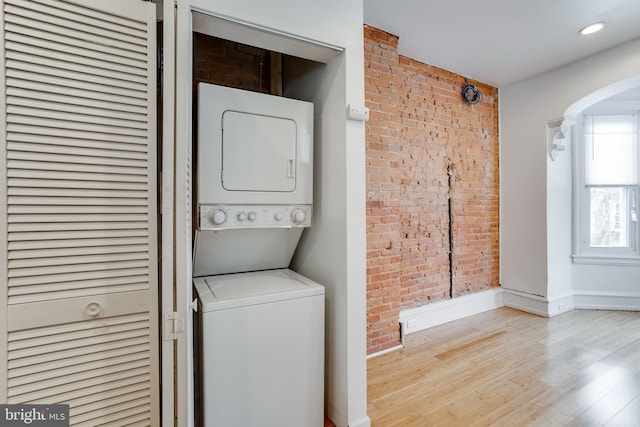 clothes washing area with stacked washer / dryer, brick wall, and light wood-type flooring