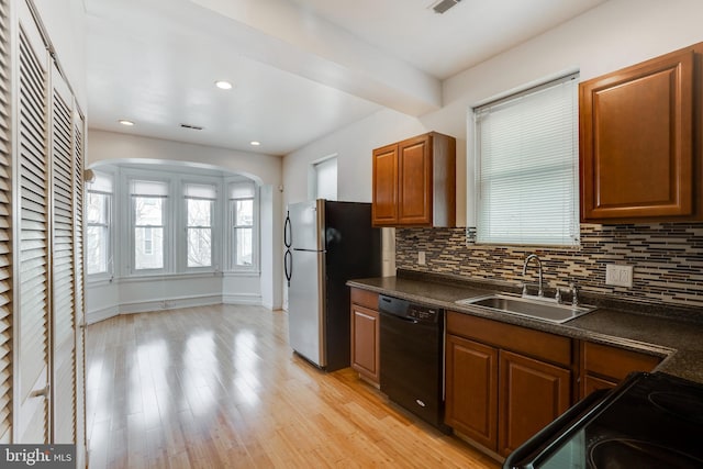 kitchen with dishwasher, sink, light wood-type flooring, stainless steel refrigerator, and tasteful backsplash