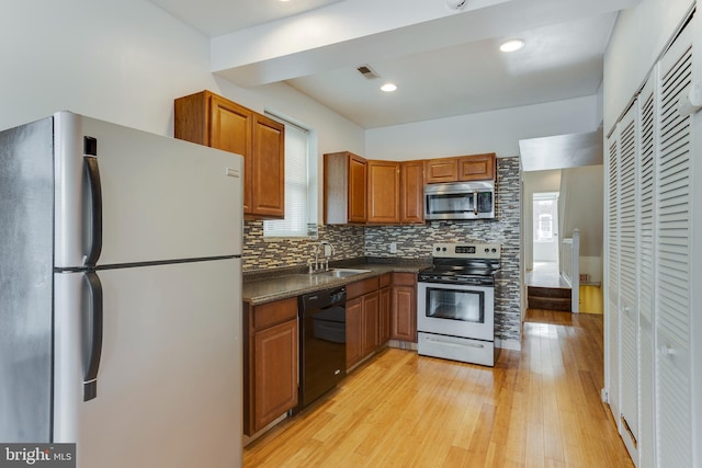 kitchen with appliances with stainless steel finishes, decorative backsplash, sink, and light hardwood / wood-style floors