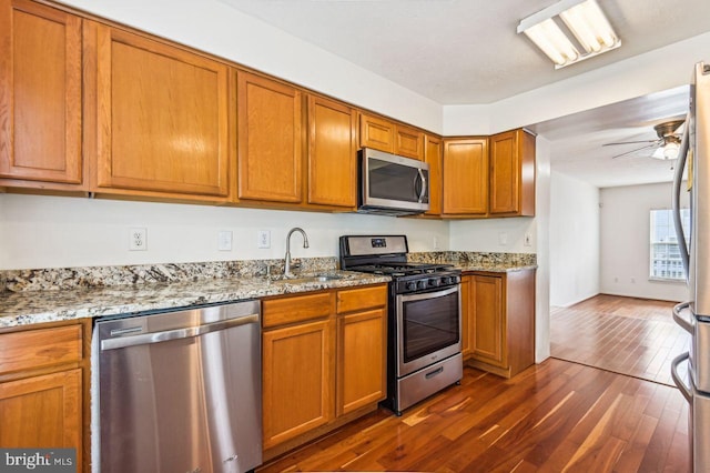 kitchen featuring dark hardwood / wood-style floors, stainless steel appliances, sink, light stone countertops, and ceiling fan