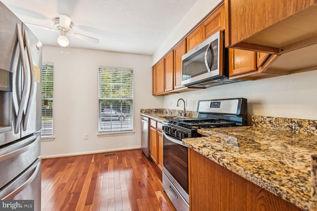 kitchen with dark wood-type flooring, stainless steel appliances, light stone countertops, and sink