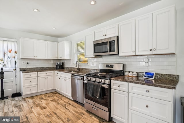 kitchen with stainless steel appliances, sink, white cabinetry, light wood-type flooring, and dark stone countertops