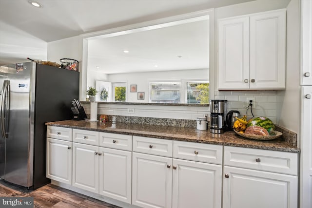 kitchen with dark hardwood / wood-style flooring, dark stone counters, stainless steel fridge, and white cabinets