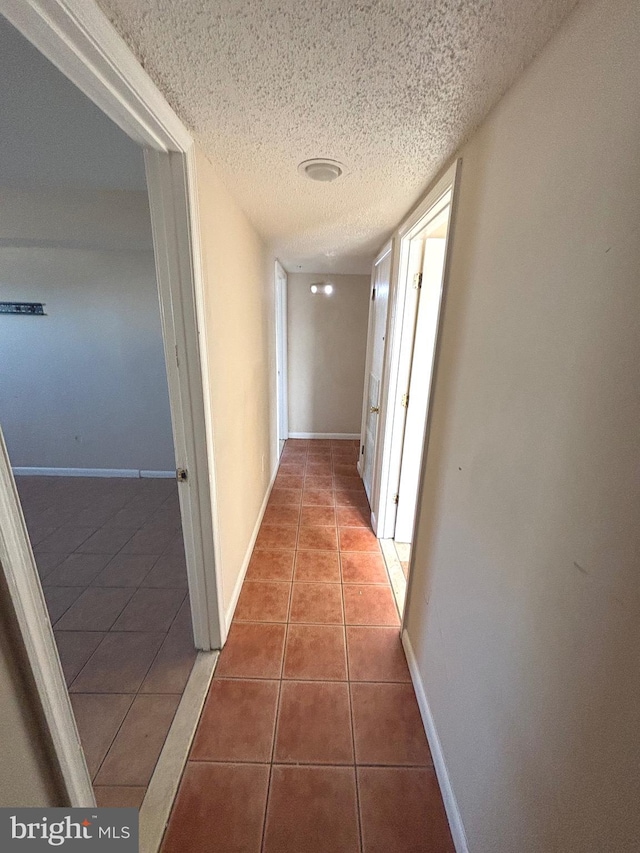 corridor with a textured ceiling and tile patterned flooring