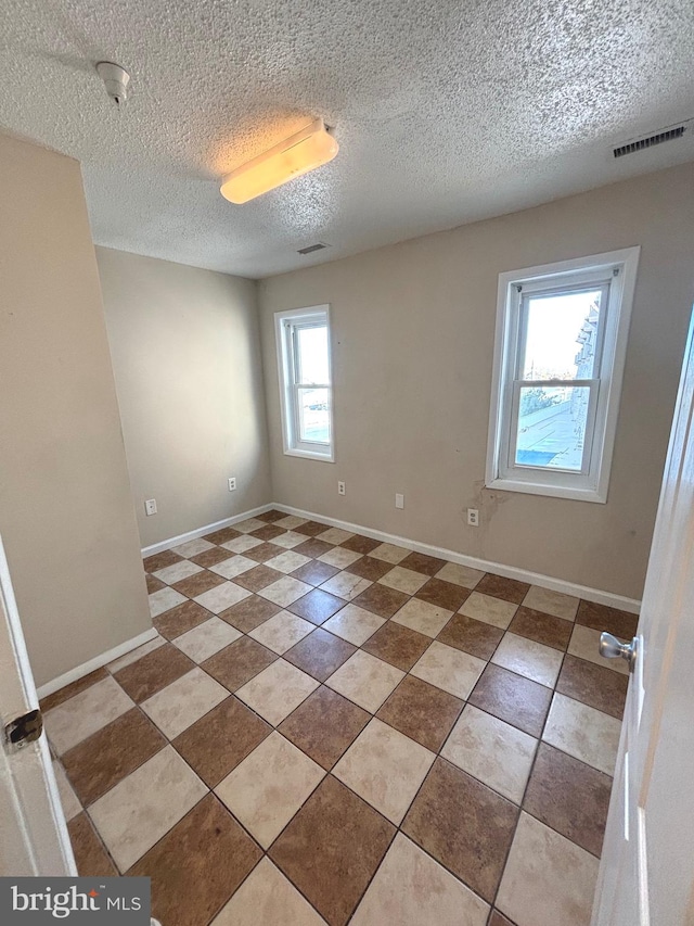 spare room with a textured ceiling, a wealth of natural light, and tile patterned flooring