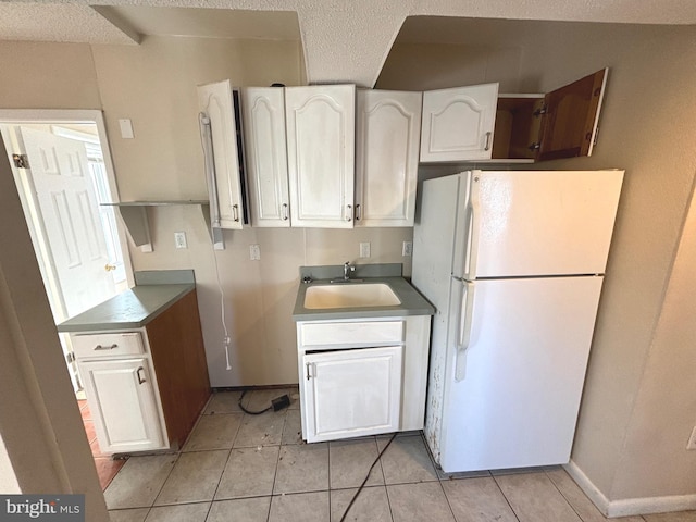 kitchen with sink, light tile patterned floors, white cabinetry, white fridge, and a textured ceiling