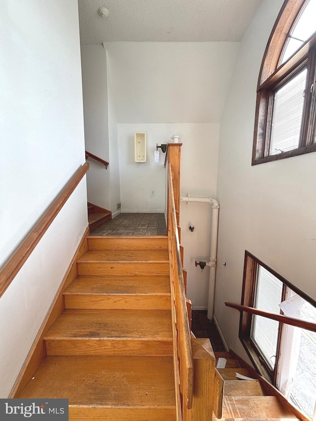 staircase featuring a healthy amount of sunlight, a textured ceiling, lofted ceiling, and hardwood / wood-style floors